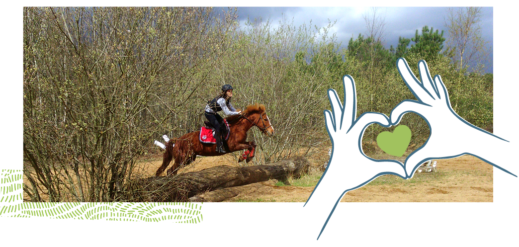 Dessin de 2 mains formant un cœur sur la photo d’une jeune cavalière sur son poney sautant un obstacle (tronc d’arbre au sol) sur un terrain sableux entouré d’arbres