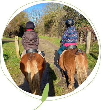 2 enfants de dos sur des poneys alezans sur un chemin de campagne en Sarthe et entouré d’arbres